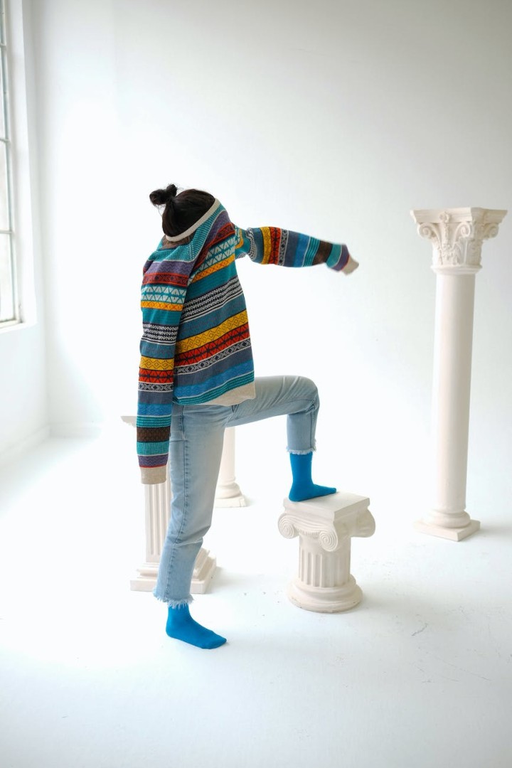 woman posing in a studio with a colorful sweater over her face