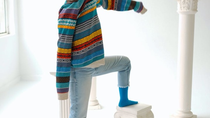 woman posing in a studio with a colorful sweater over her face